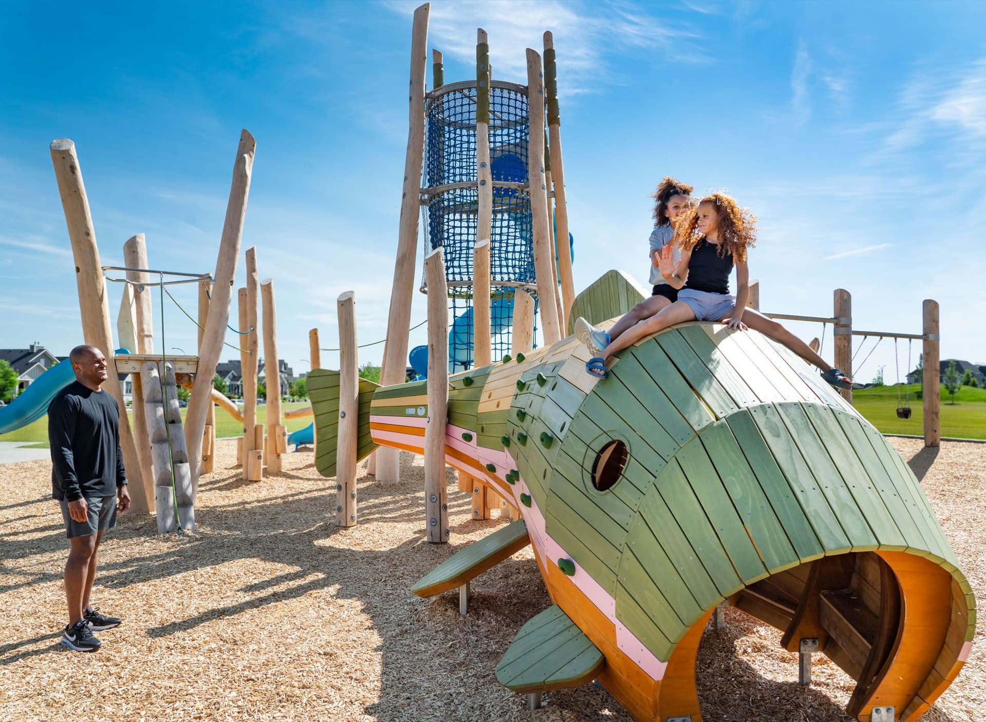 Two girls wave at their father from a fish-shaped play structure at Mahogany Central Green.